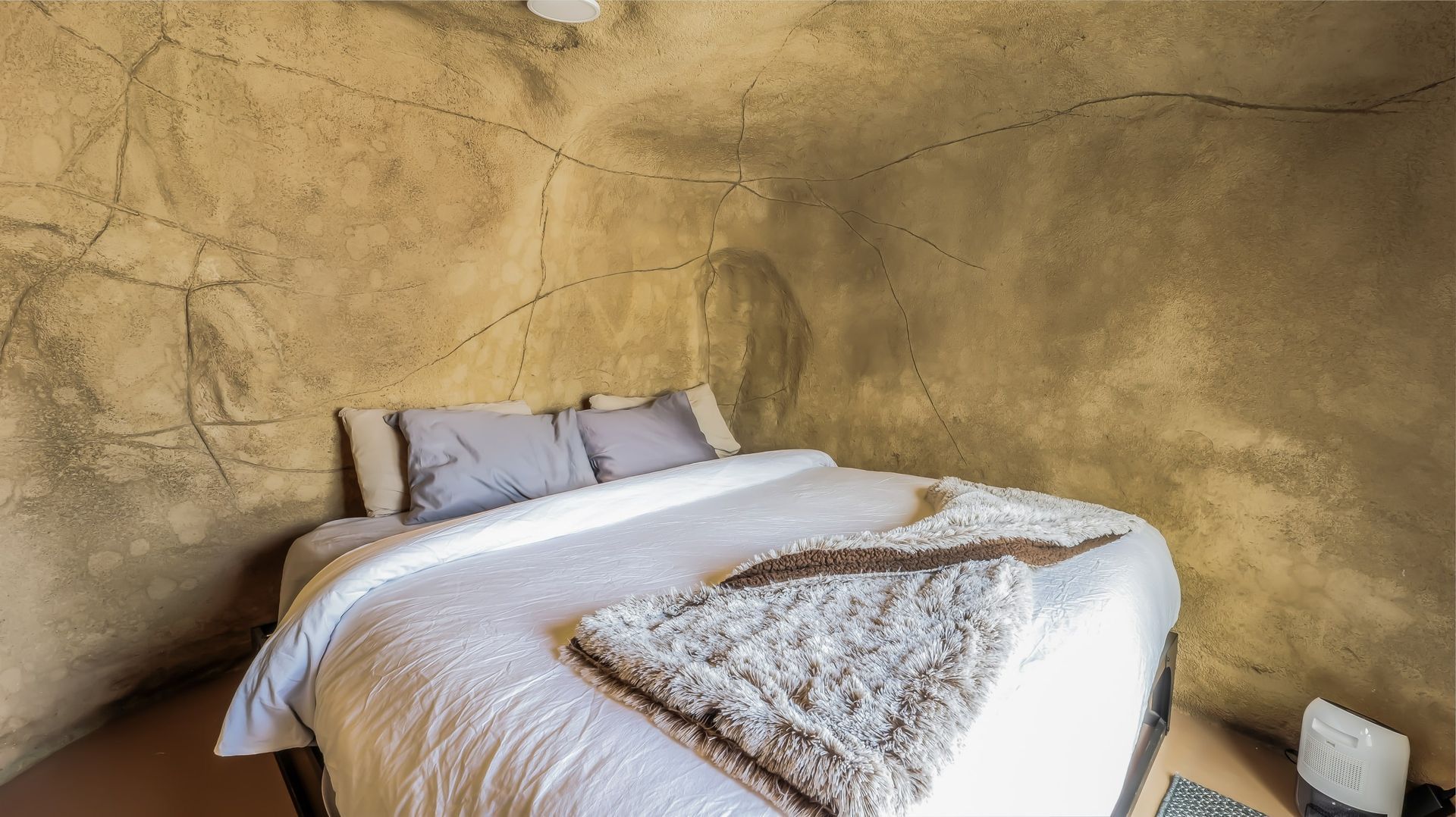 A bed with white sheets and pillows in a room with a rock wall.