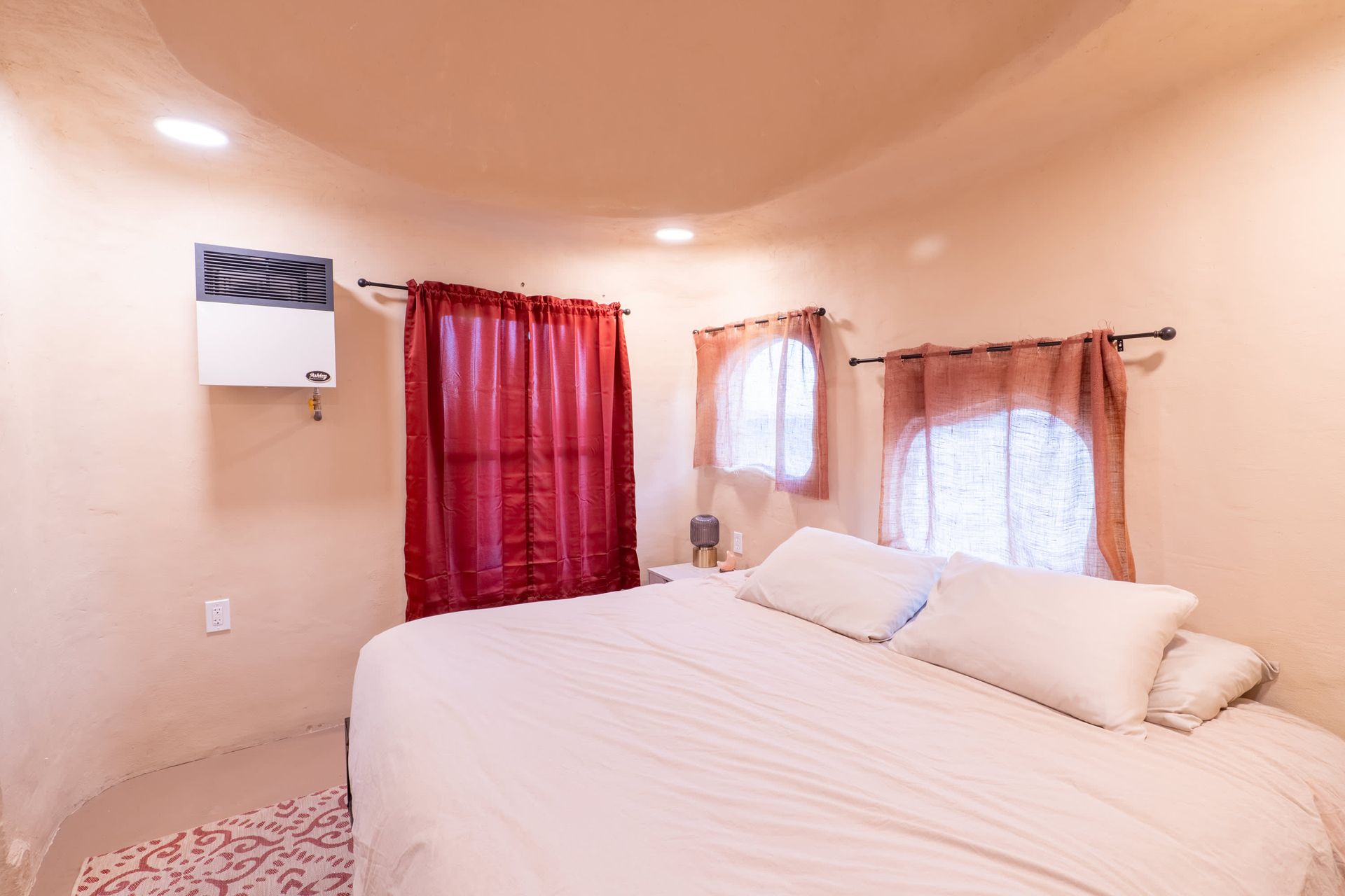 A bedroom with a bed and two windows with red curtains.