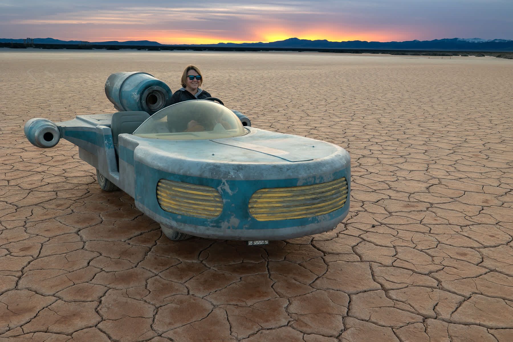 A person is driving a futuristic car in the middle of a desert.