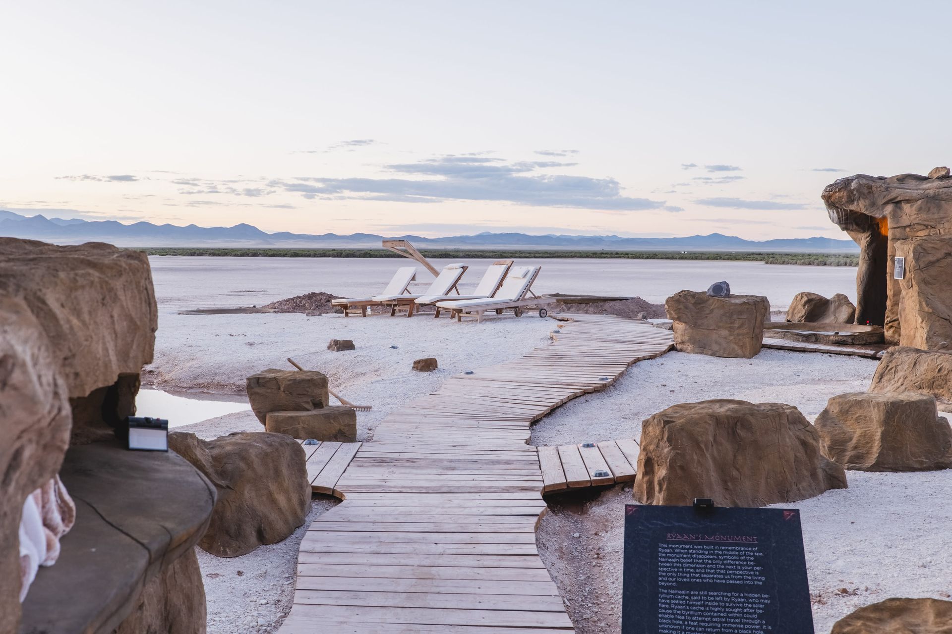 A wooden walkway leading to a large body of water surrounded by rocks.