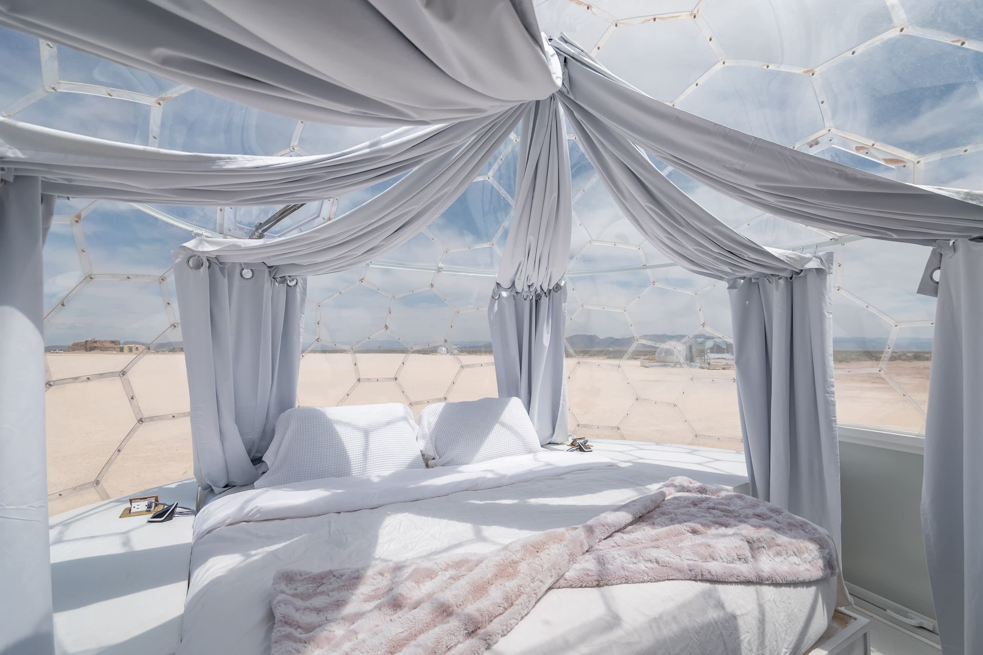 A bed in a dome with white curtains and a view of the desert.