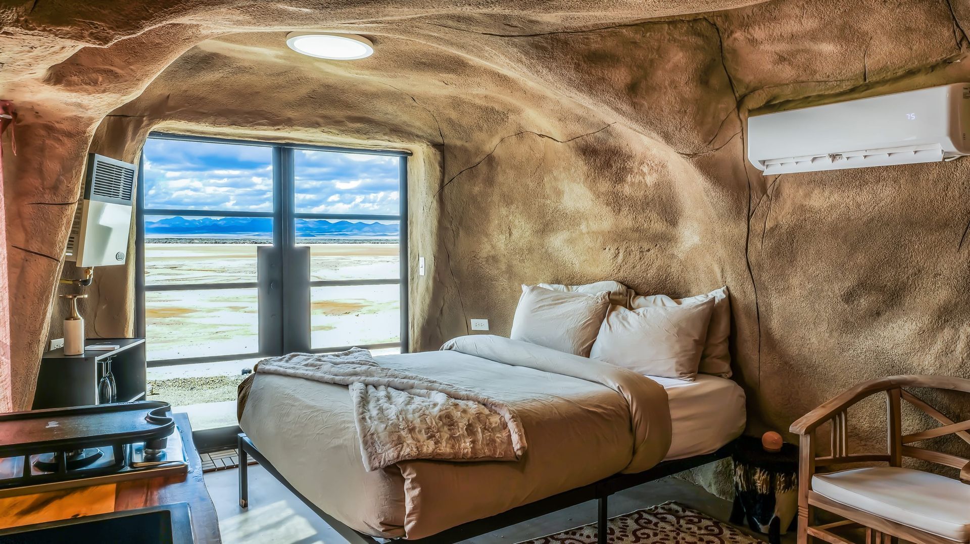 A bedroom in a cave with a bed and chairs.