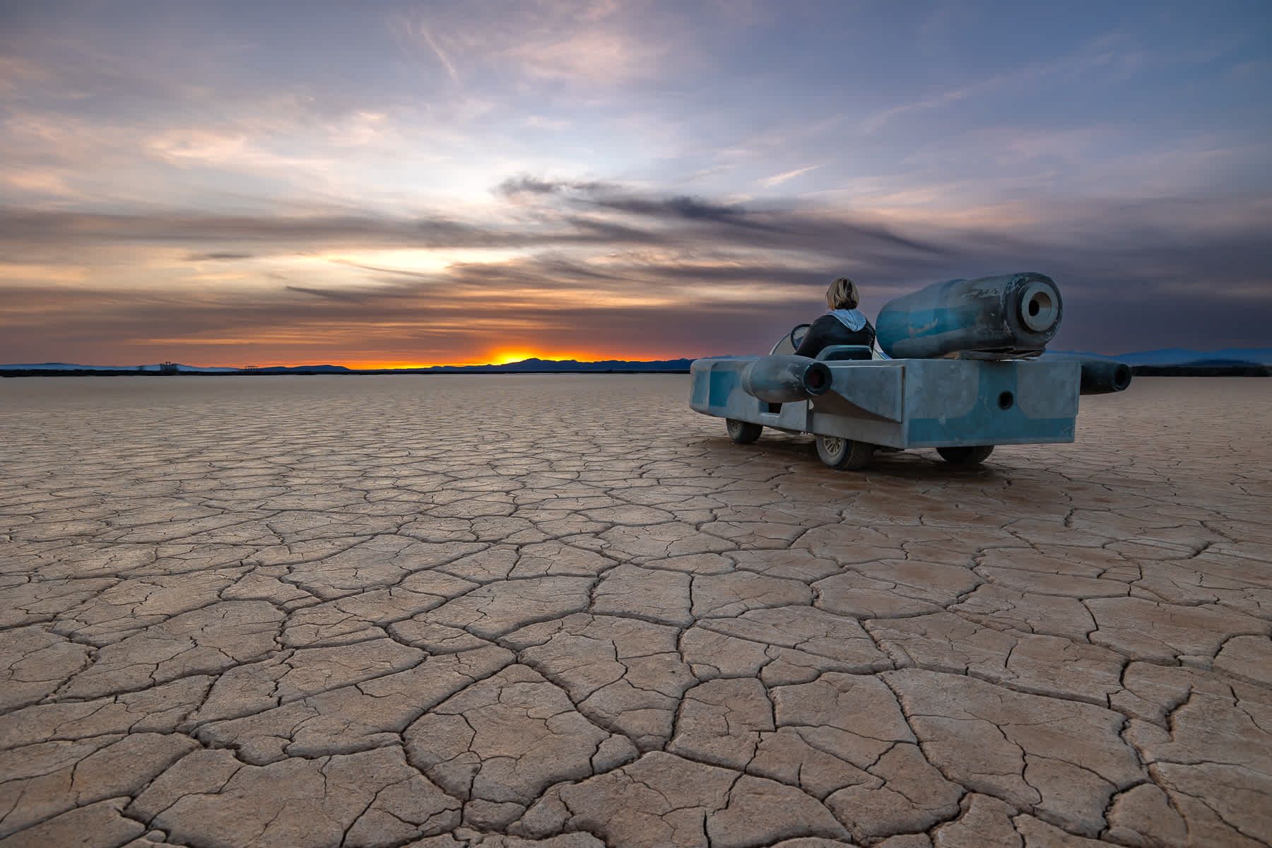 A person is sitting in a toy car in the middle of a desert.