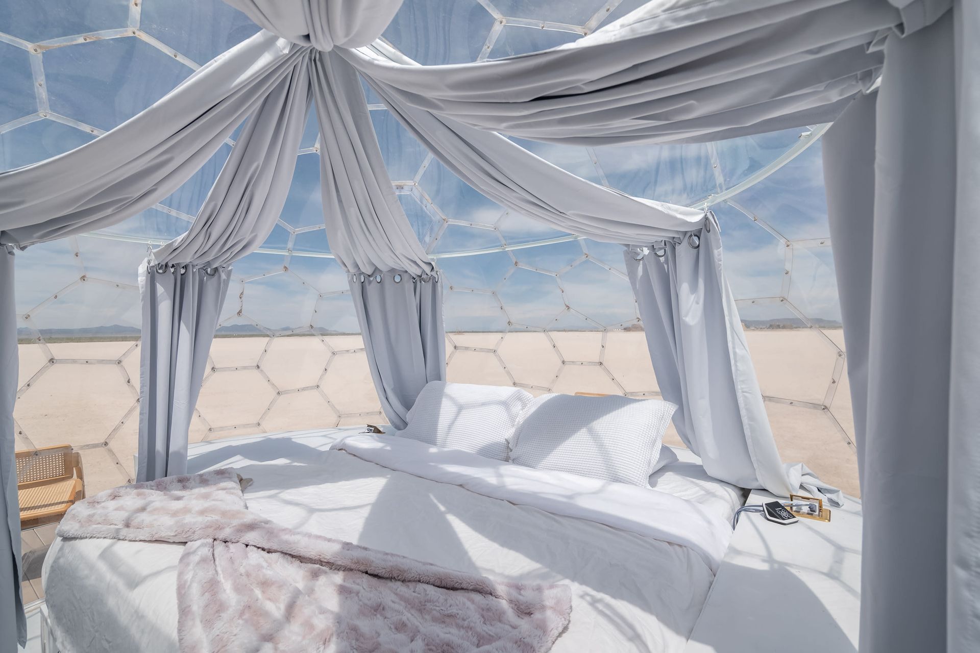 There is a bed in the middle of a dome with white curtains.