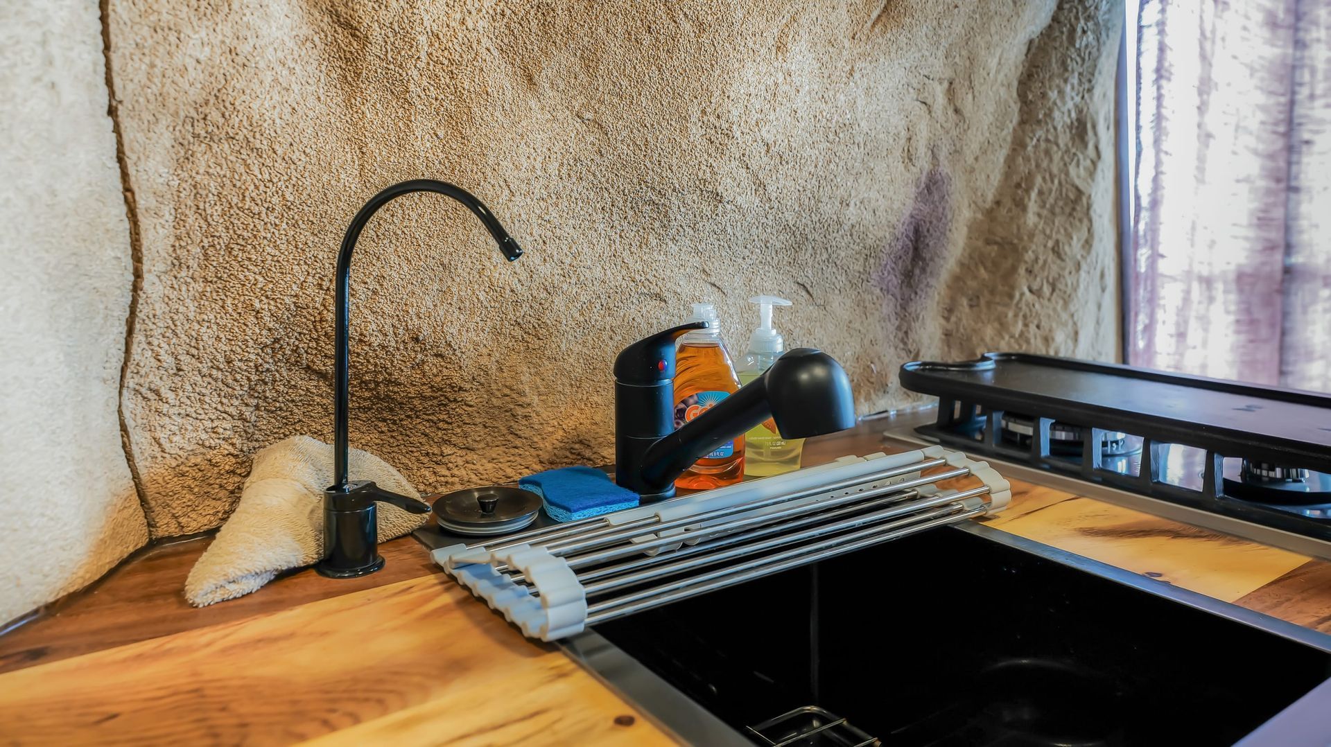 A kitchen sink with a faucet and a soap dispenser on a wooden counter.