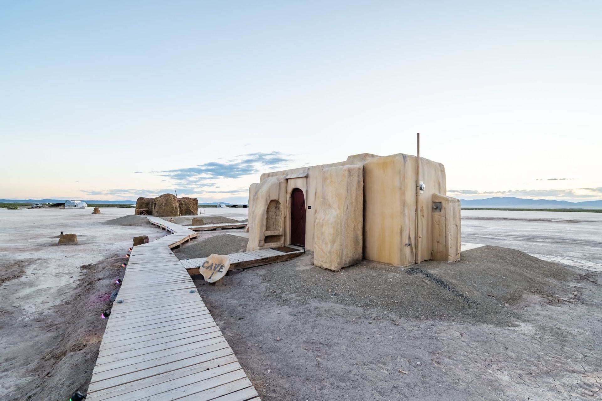 A wooden walkway leading to a building in the middle of a desert.
