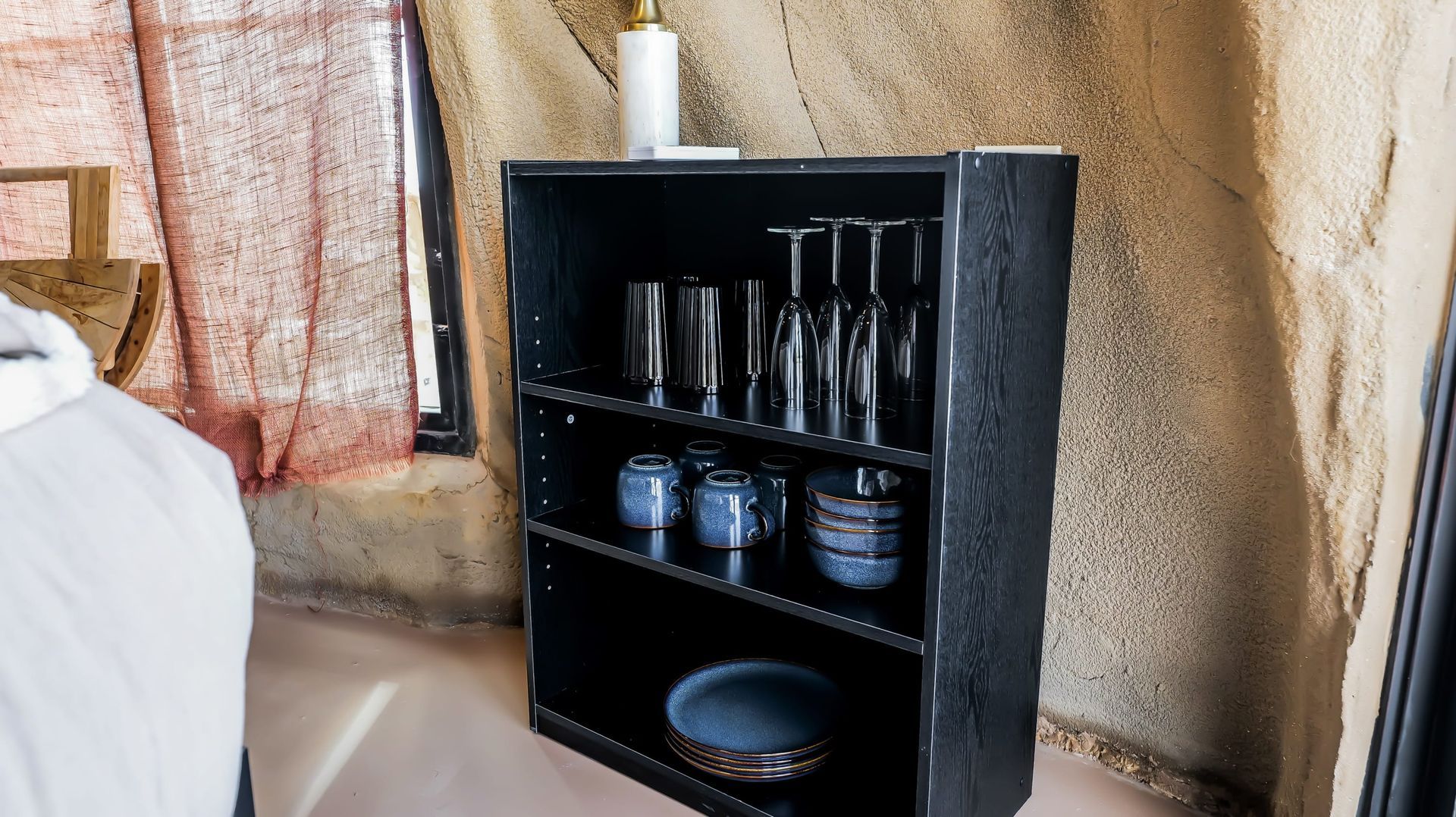 A shelf with glasses , bowls , and plates on it in a room.