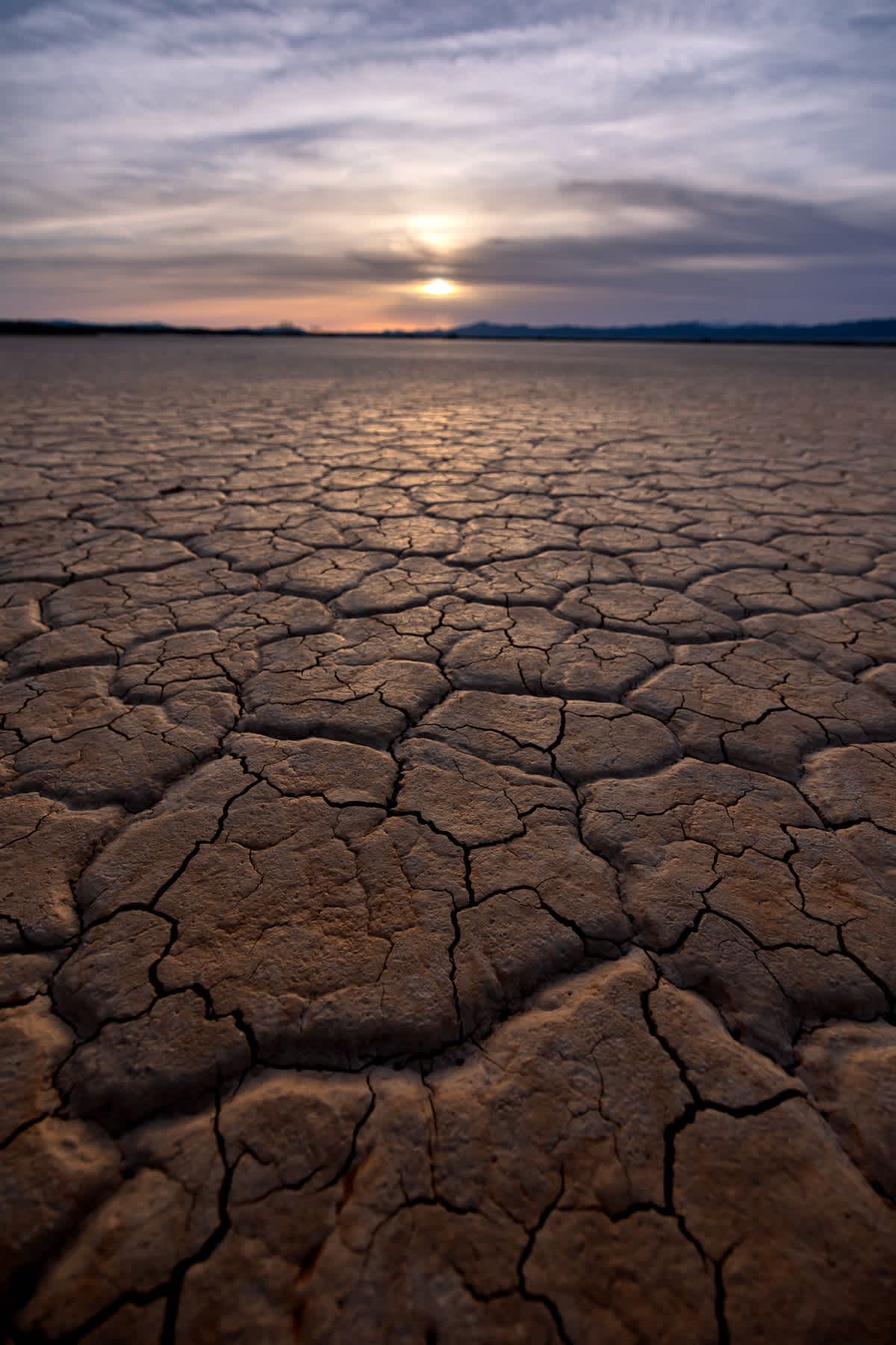 The sun is setting over a dry cracked desert landscape.
