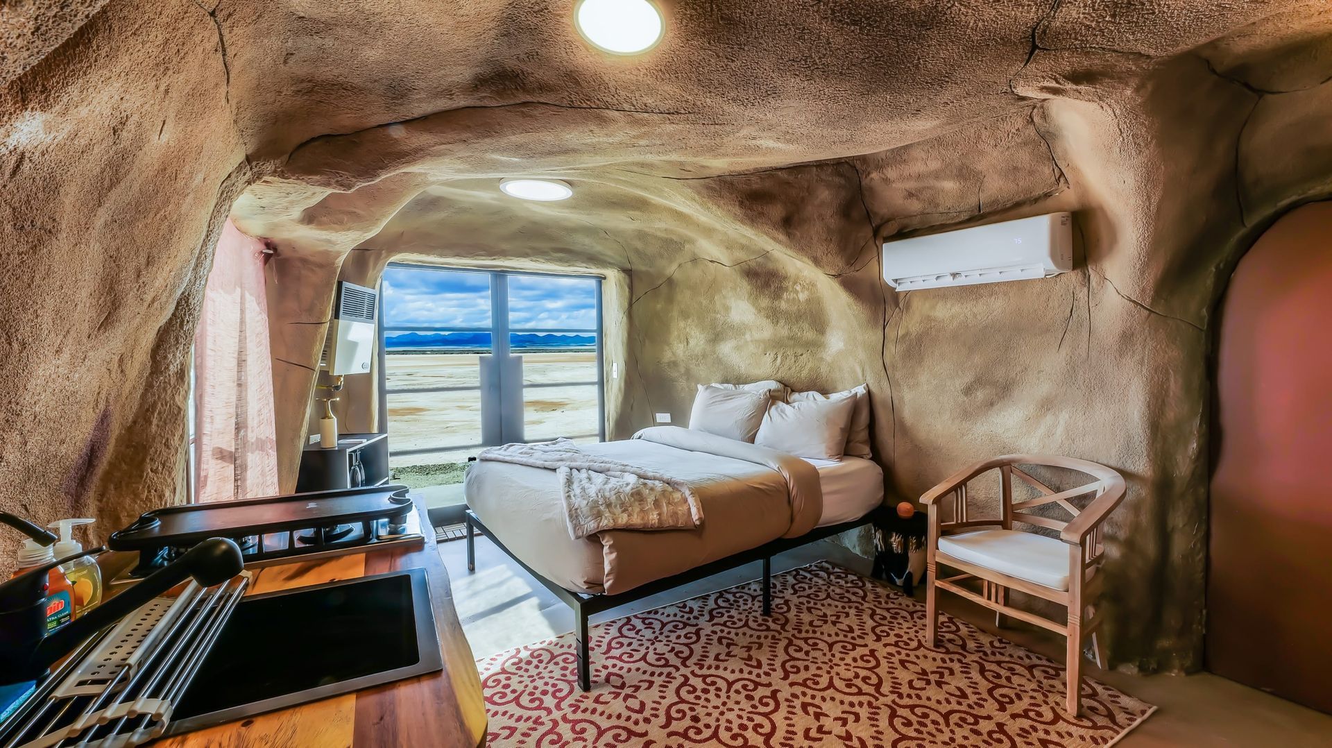 A bedroom in a cave with a bed and chairs.