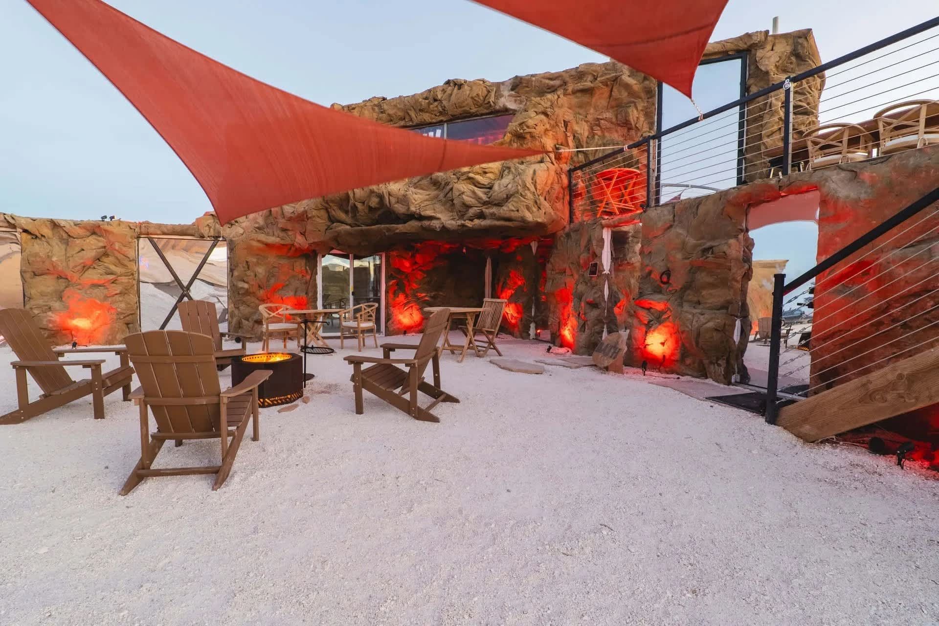 A patio with chairs and a fire pit under red umbrellas.