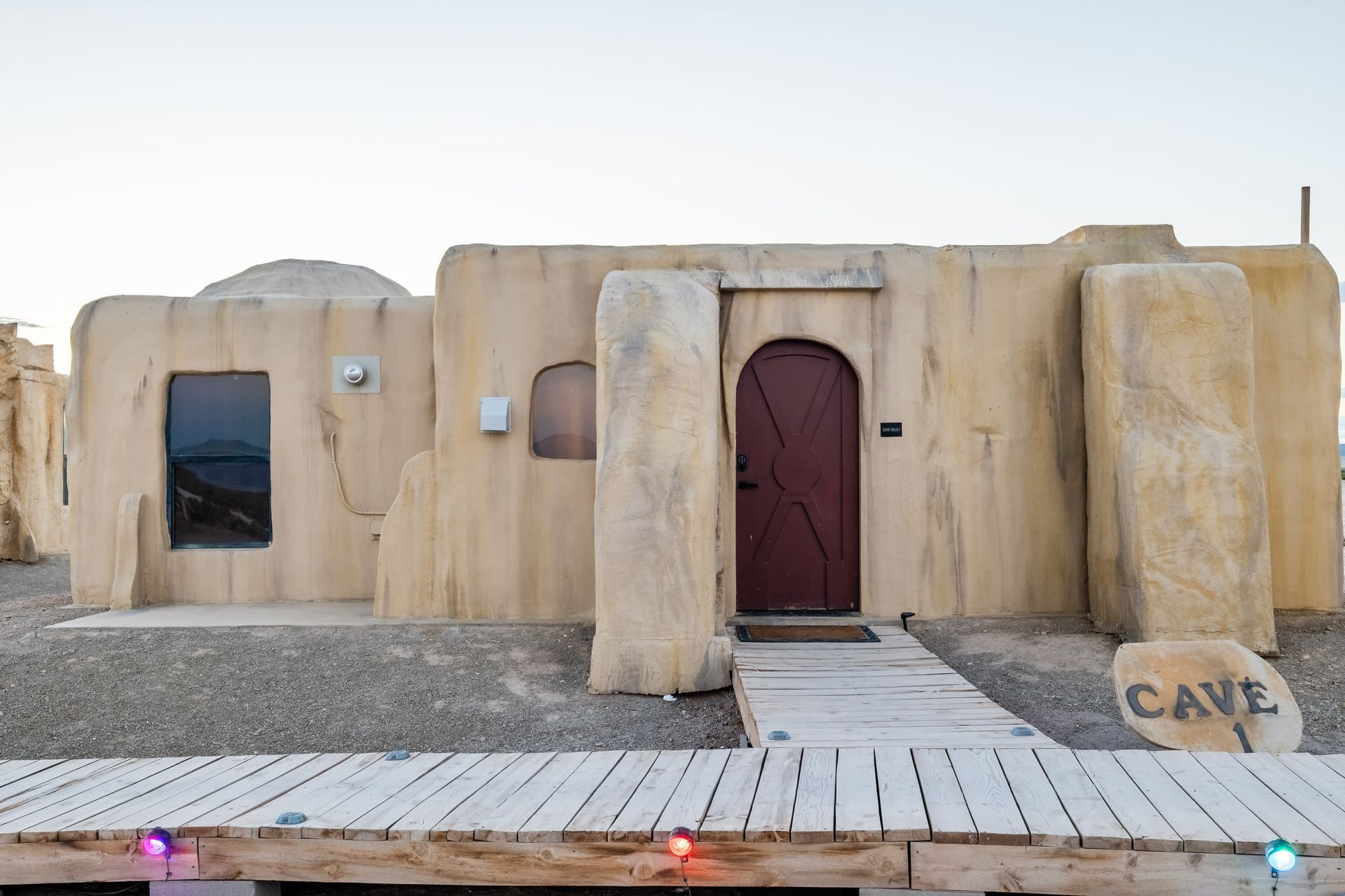 A desert house with a red door and a wooden walkway leading to it.