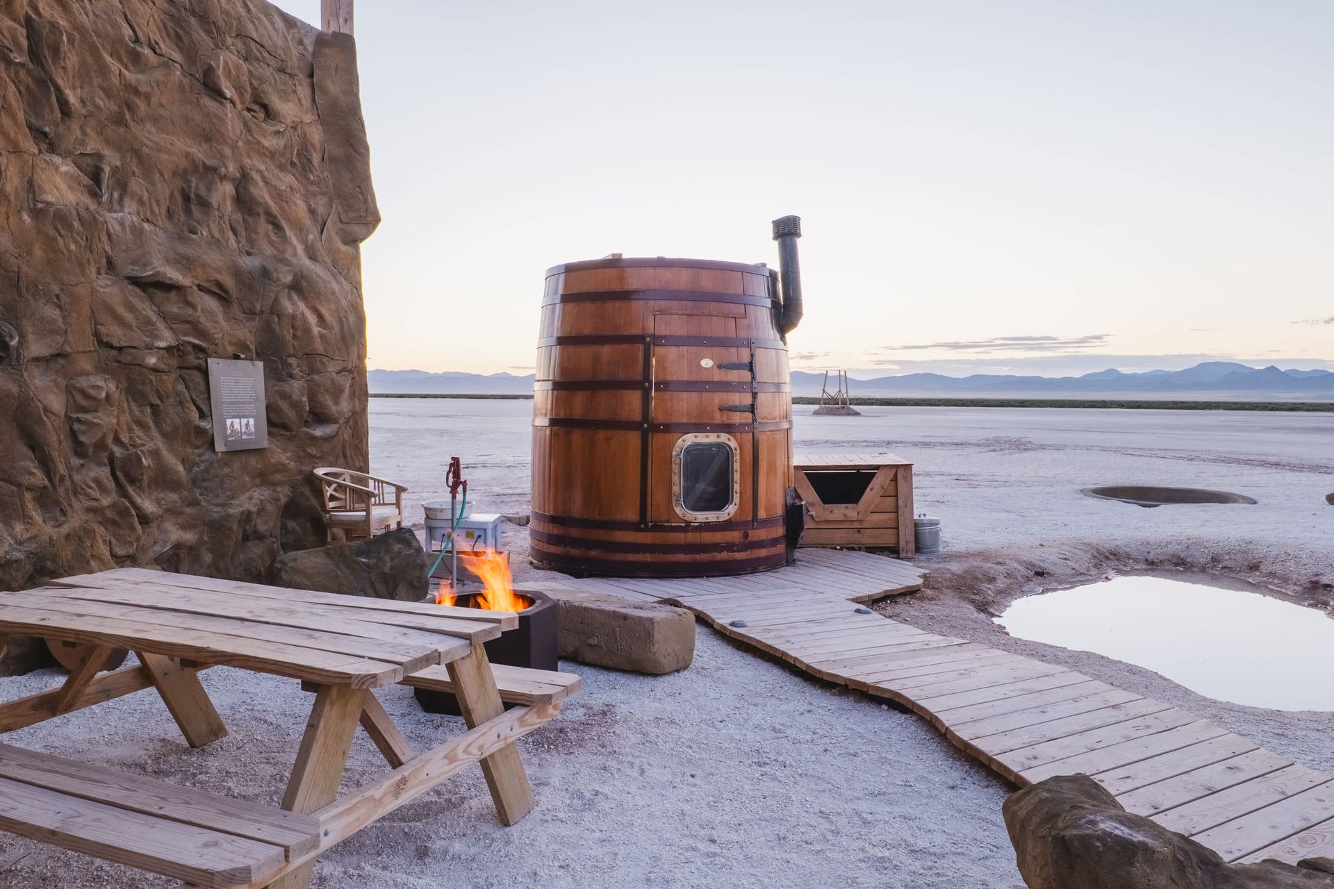 A wooden barrel is sitting next to a wooden picnic table.