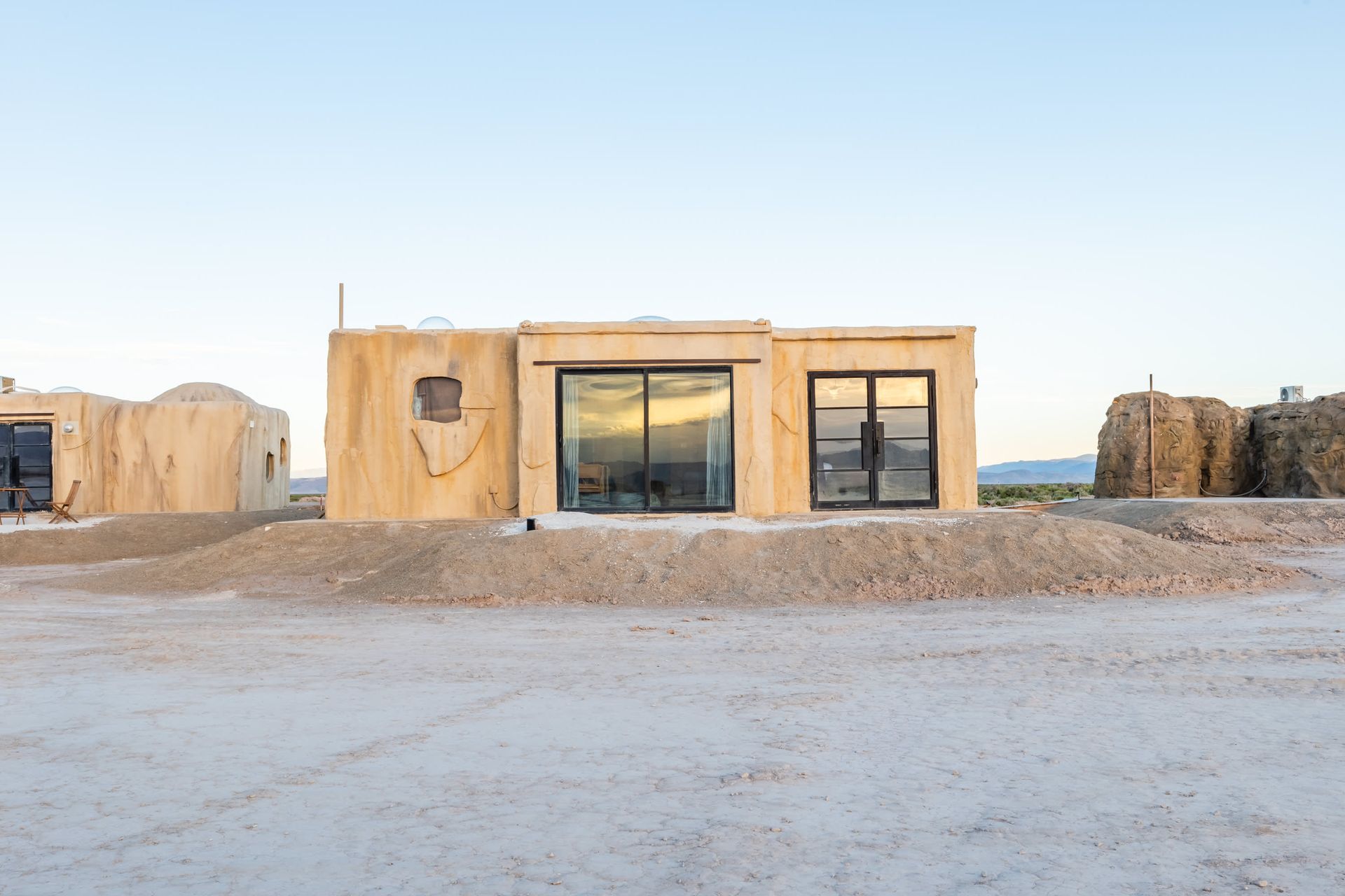 A small house is sitting in the middle of a dirt field.