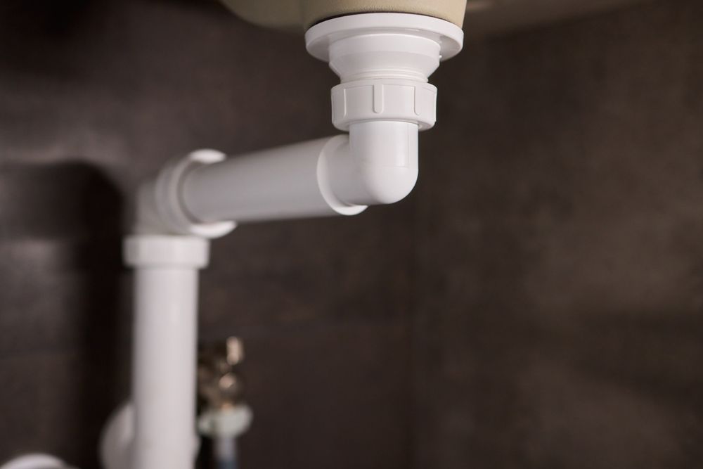 White plumbing pipes under a sink.  Elbow joint and vertical drain pipe visible. — Vantage Plumbing and Drainage In Mudgereeba, QLD