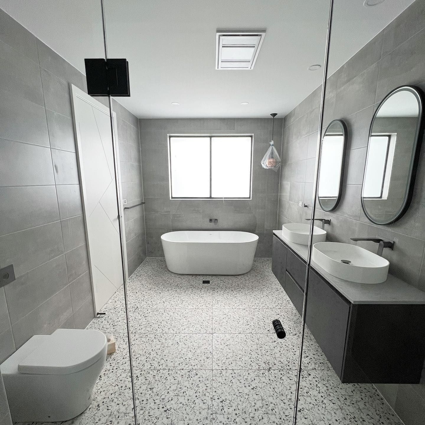 Modern bathroom with white bathtub, dual sinks, and light gray tile walls. — Vantage Plumbing and Drainage In Pacific Pines, QLD