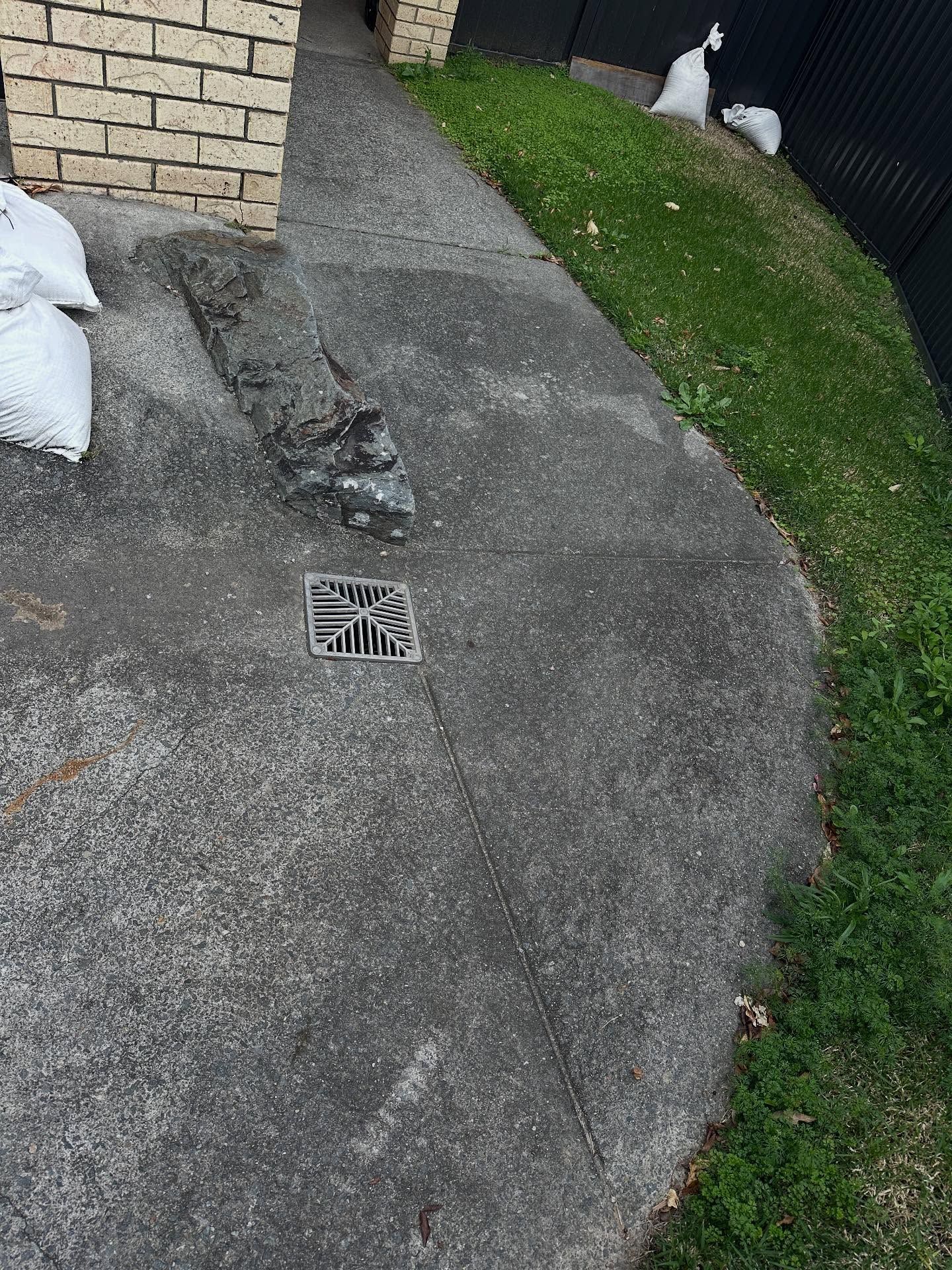 Concrete Driveway With a Drain, Brick Wall, Grass, and Bags — Vantage Plumbing and Drainage In Pacific Pines, QLD