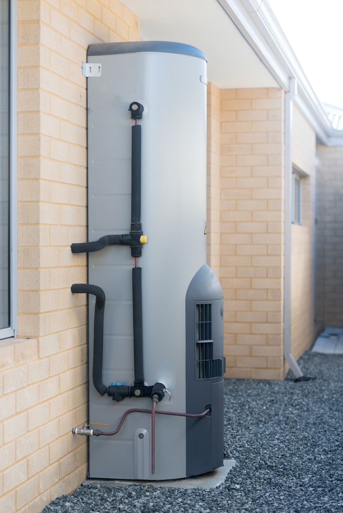 Tall, grey water heater outside a brick building. Black pipes connect to the tank. — Vantage Plumbing and Drainage In Nerang, QLD