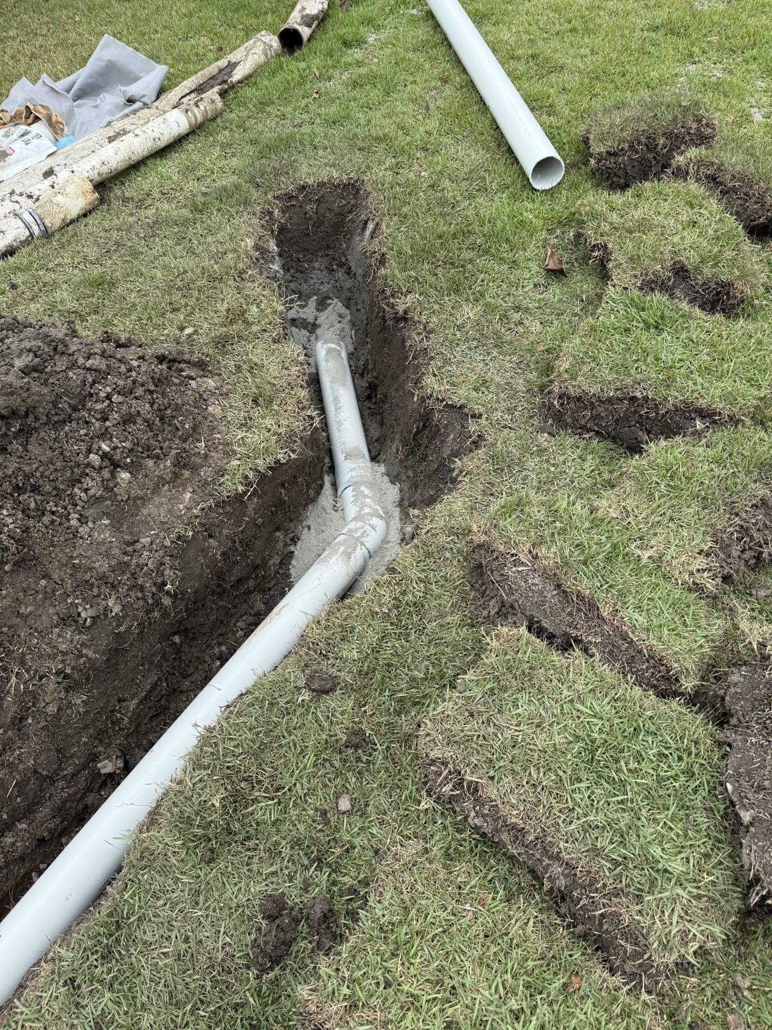 A Trench With Installed Gray PVC Pipes in a Grassy Yard — Vantage Plumbing and Drainage In Pacific Pines, QLD