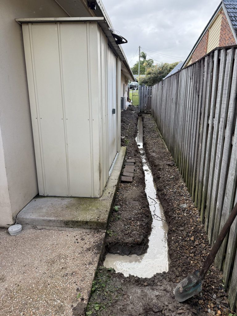 Narrow Trench Dug Beside a Building and Fence, Filled With Wet Concrete — Vantage Plumbing and Drainage In Pacific Pines, QLD