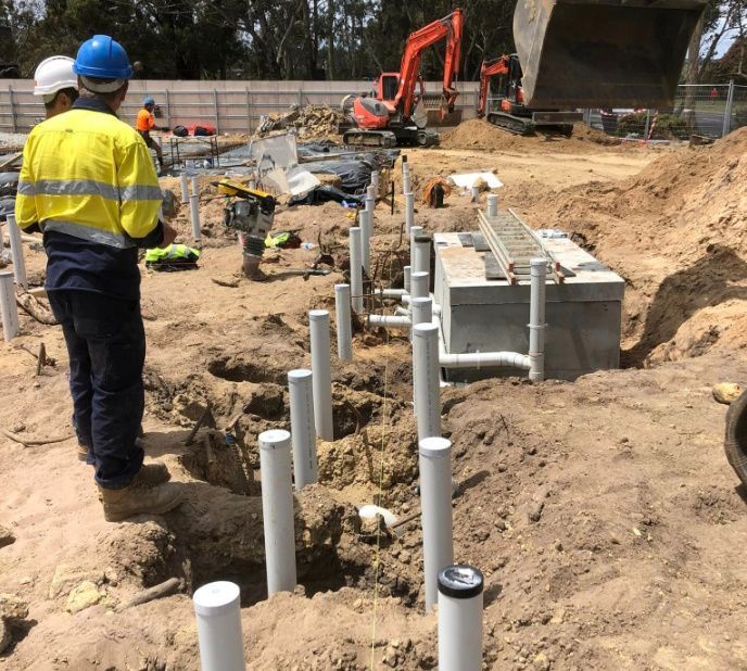 Construction site with workers, pipes, and machinery. One worker in a yellow safety vest observes plumbing installation. — Vantage Plumbing and Drainage In Pacific Pines, QLD