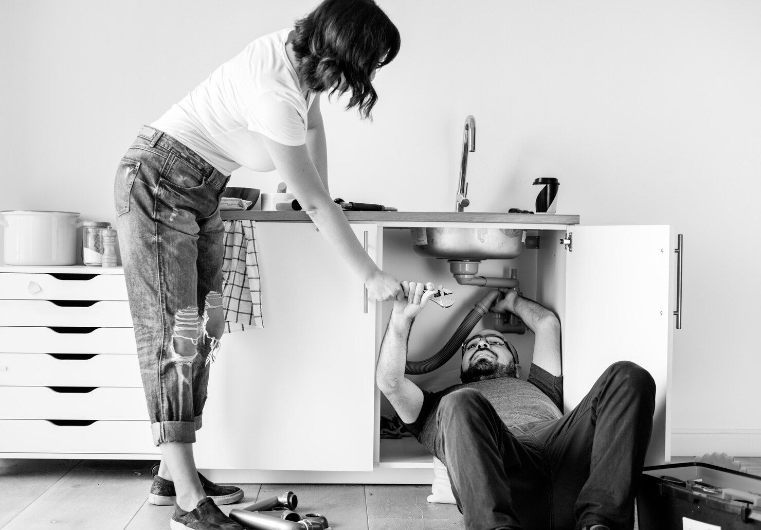 Woman Helps Man Working on Plumbing Under a Sink — Vantage Plumbing and Drainage In Pacific Pines, QLD