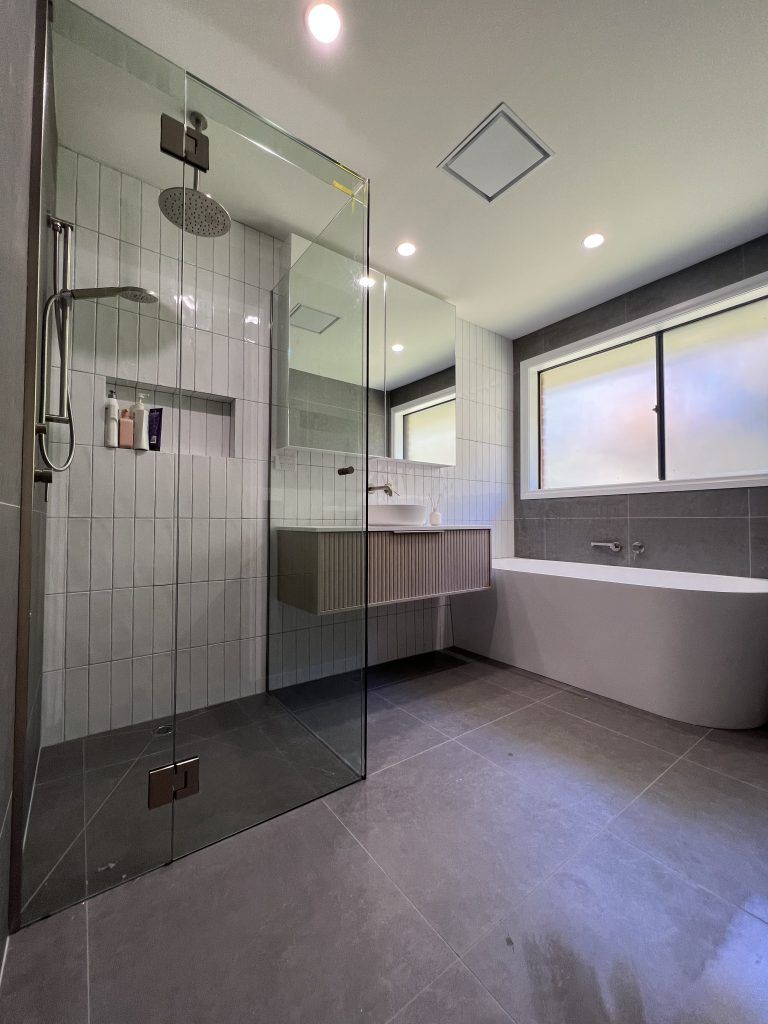 Bathroom With Grey Tiles, Glass Shower and Freestanding Tub — Vantage Plumbing and Drainage In Pacific Pines, QLD