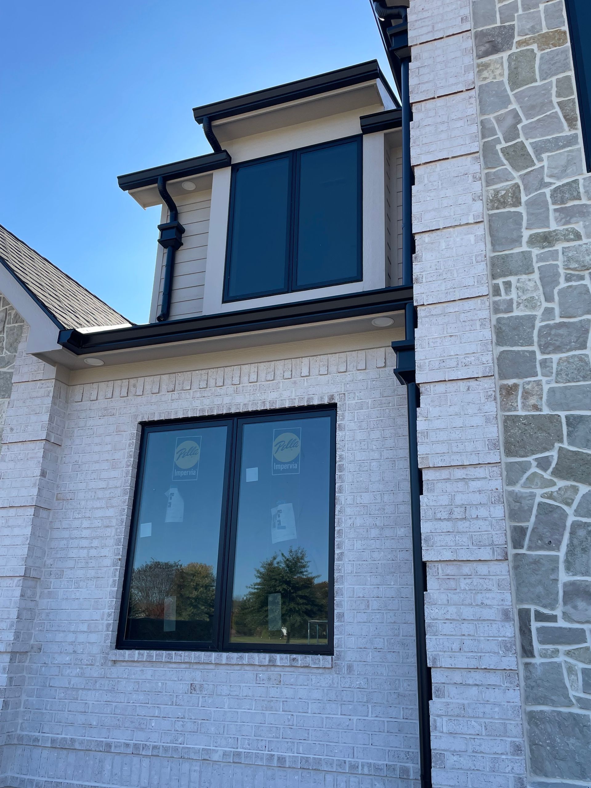 Brick house exterior with black-framed windows and dark gutters, set against a bright sky.