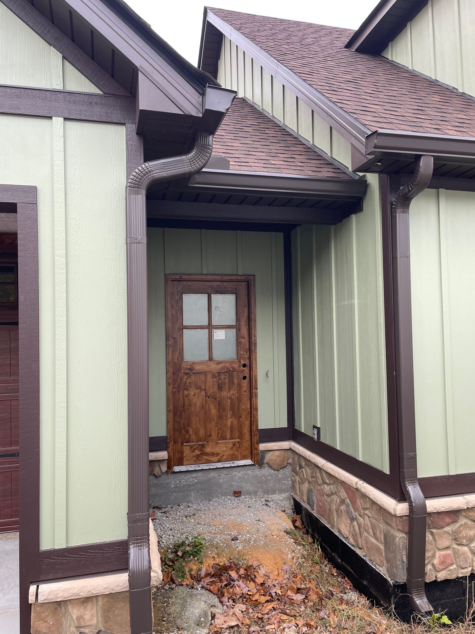 Brown wooden door set into light green wall of a building with brown trim and a gutter.