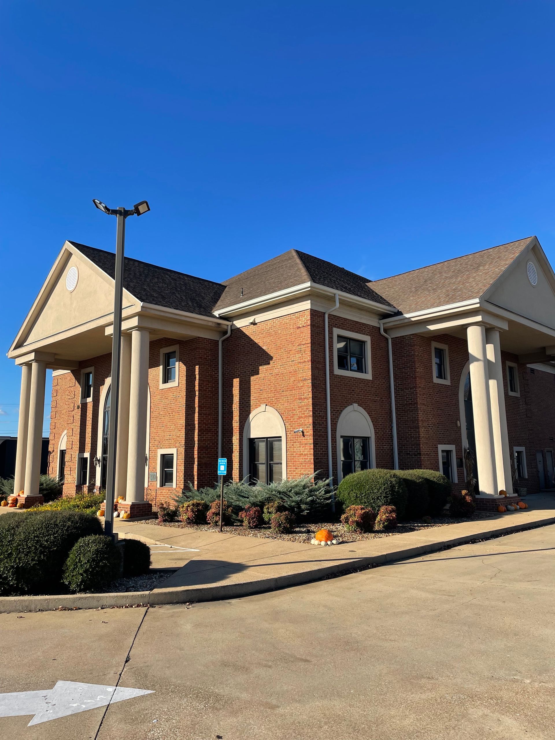 Brick building with columns, blue sky, and parking area.
