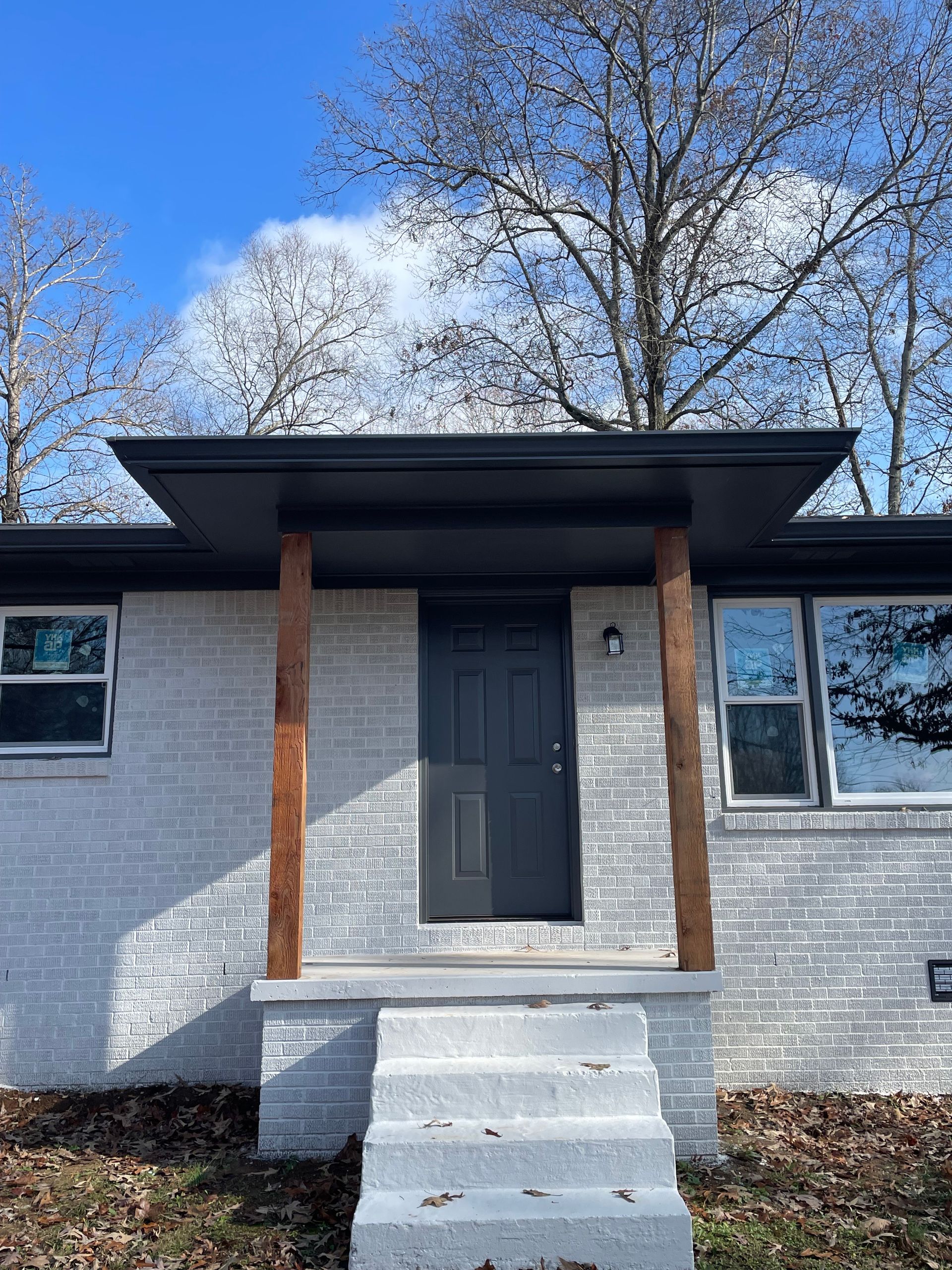 A house with a gray brick facade, black door, and wooden columns supporting a dark canopy.