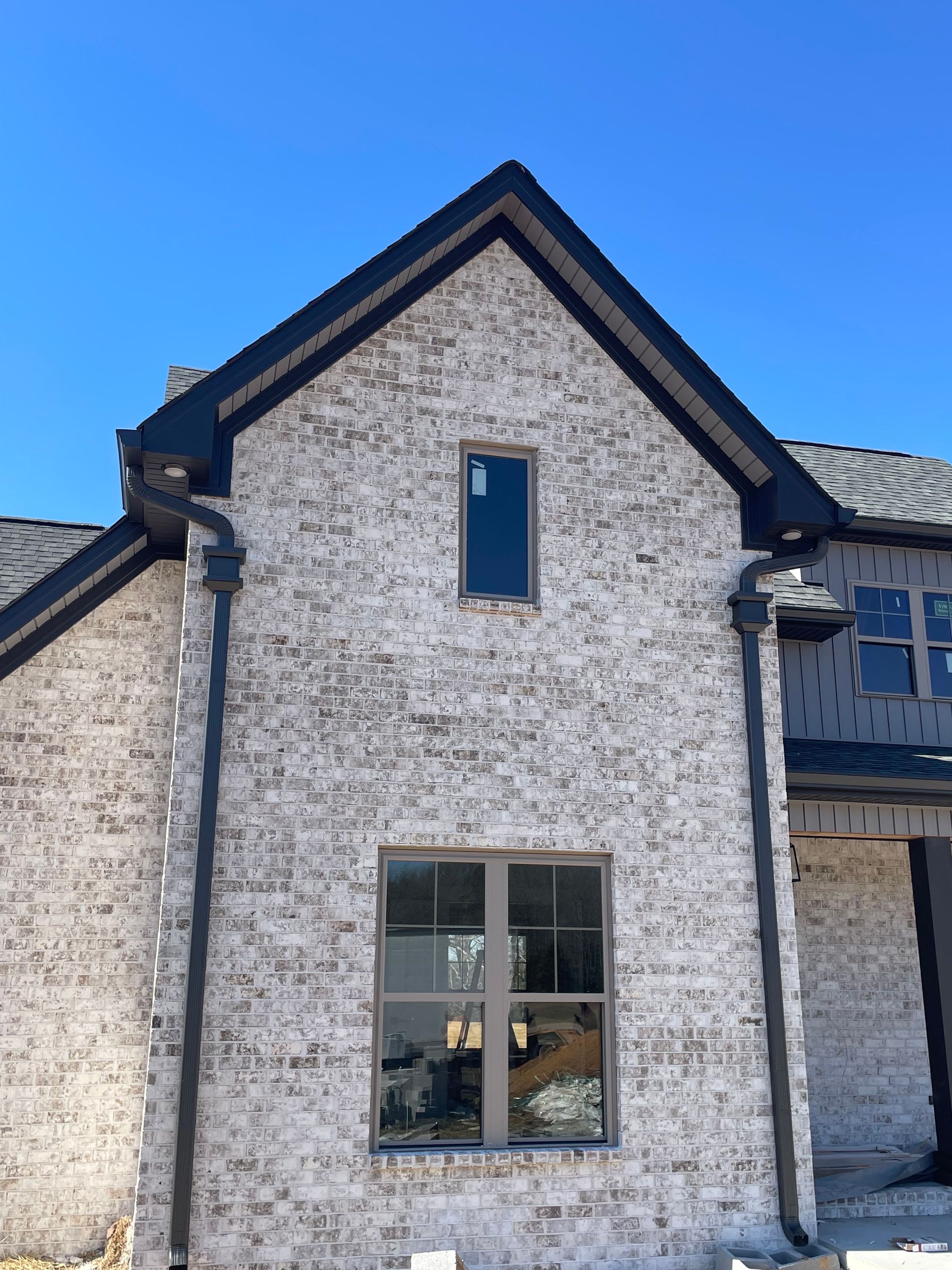 Brick house with dark trim, windows, and gutters against a blue sky.
