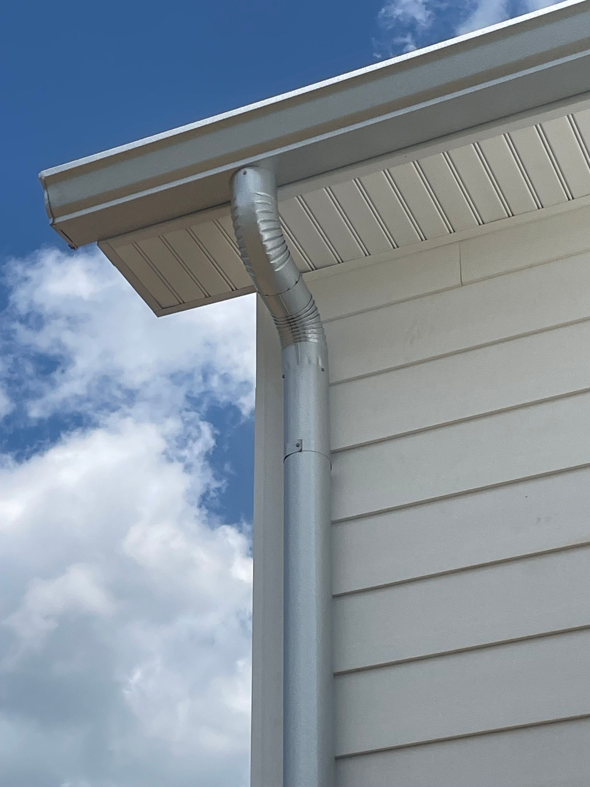 Silver gutter system on a white house, against a blue sky with clouds.