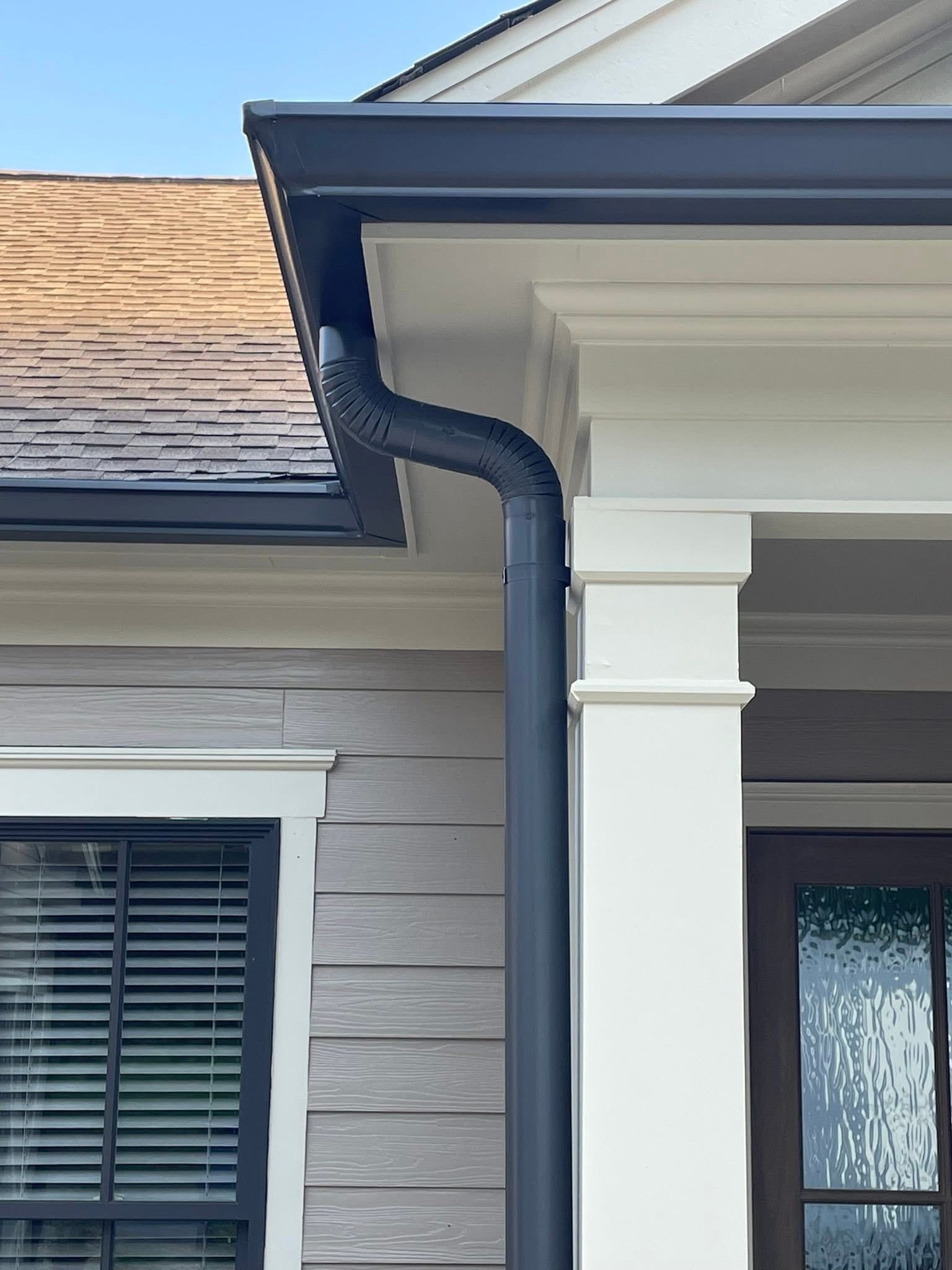 Dark blue gutter and downspout on a house with gray siding, white trim, and a brown roof.