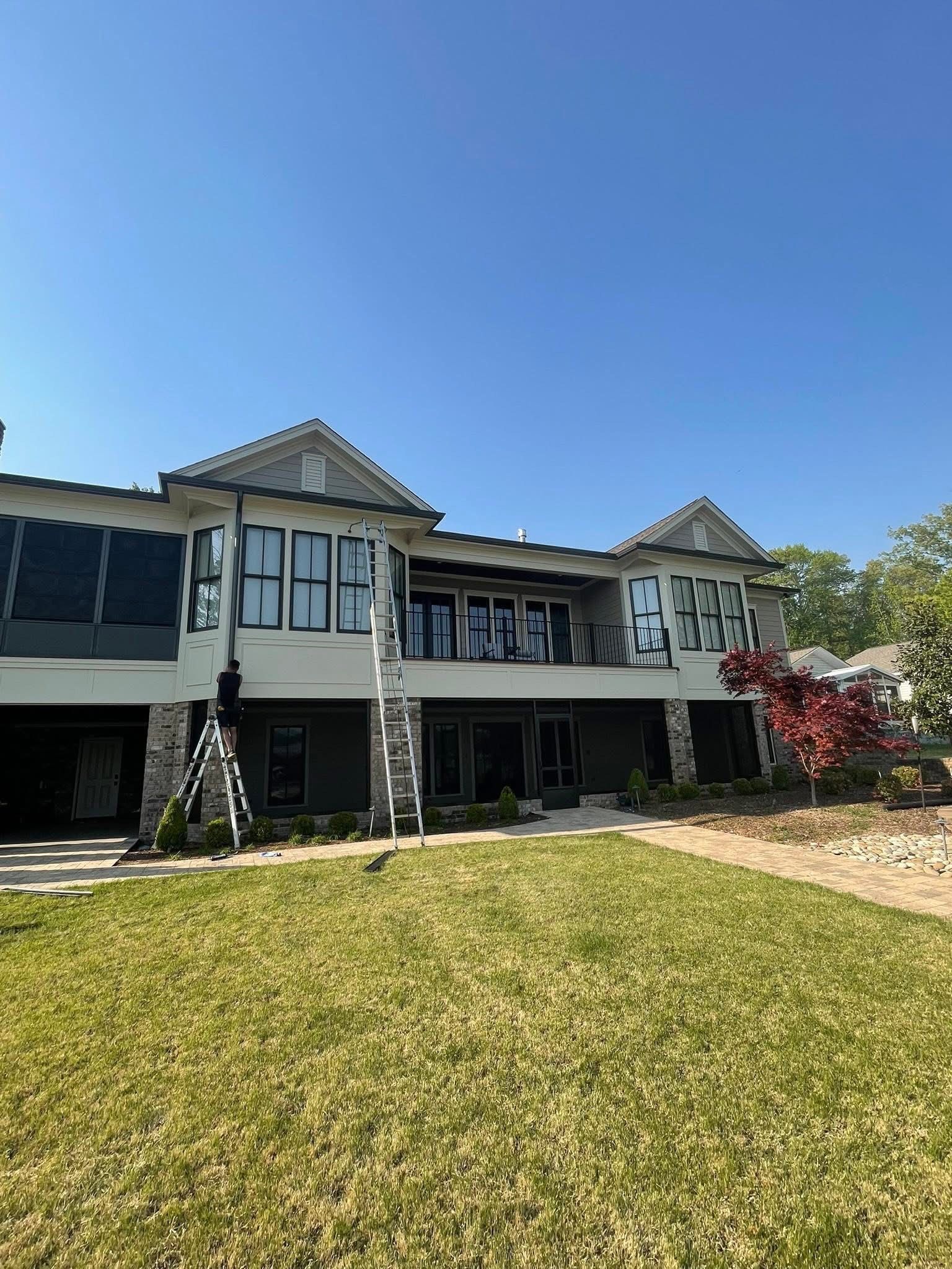 House under construction with exposed walls and dark window frames, lawn in foreground, clear sky.