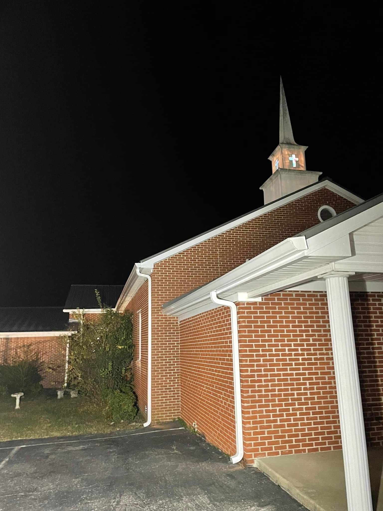 Brick church at night, steeple with cross, dark sky.