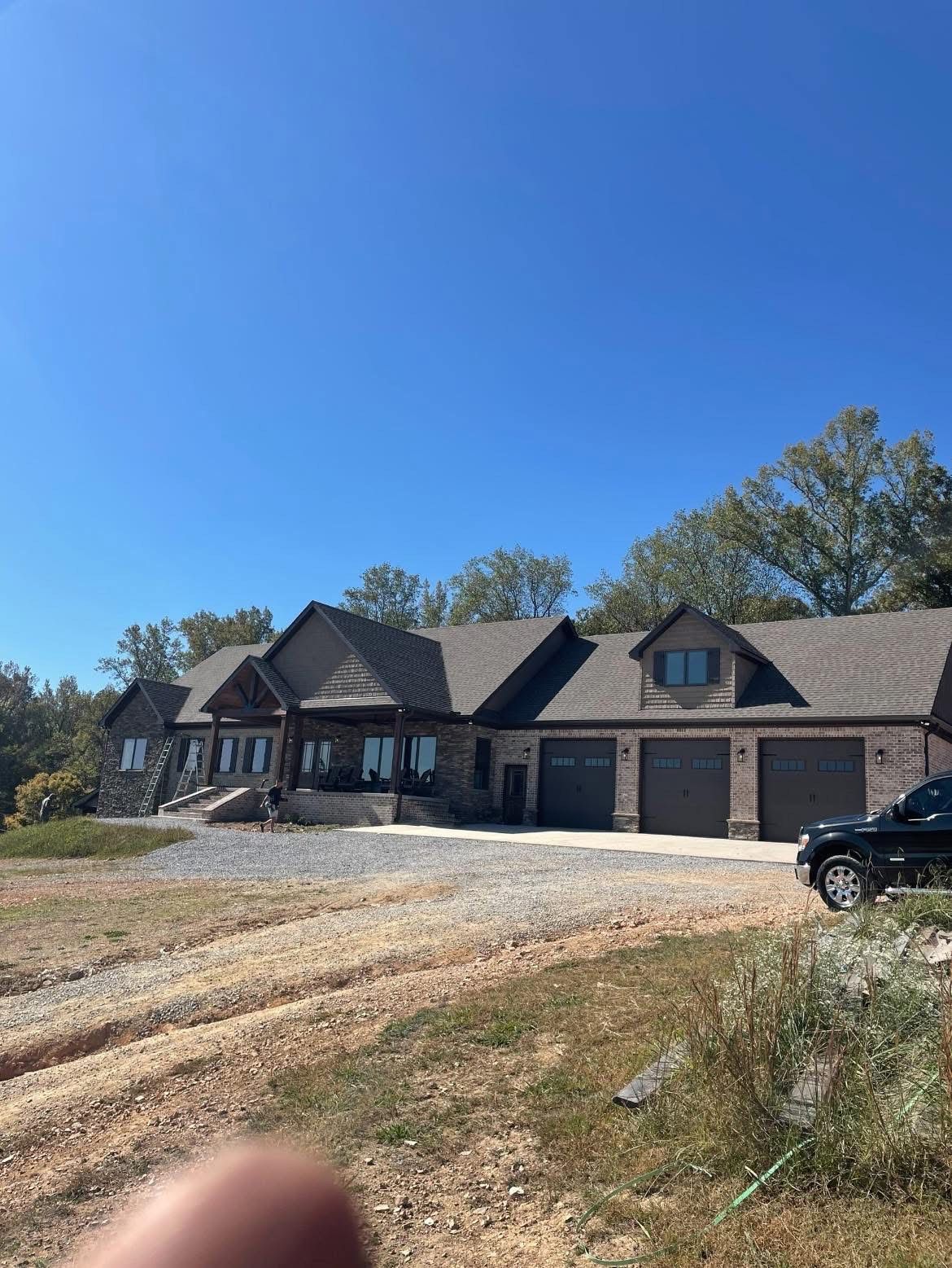 Large brick and wood-sided house with a three-car garage and long driveway, under a bright blue sky.