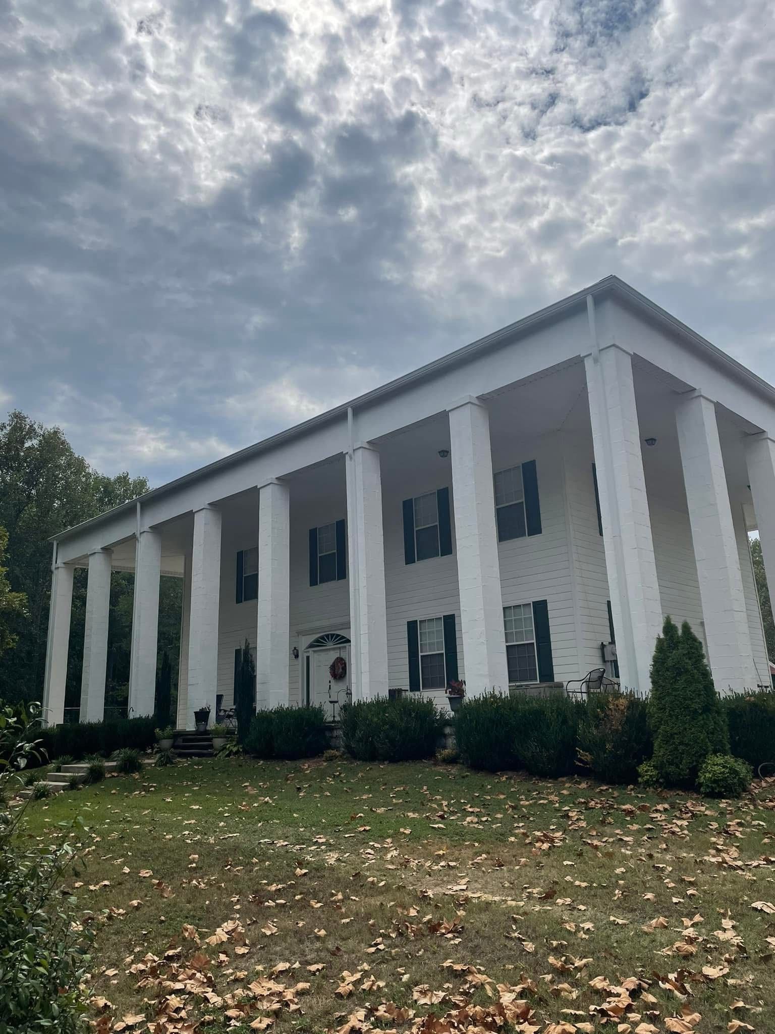 White two-story house with large columns and a cloudy sky.