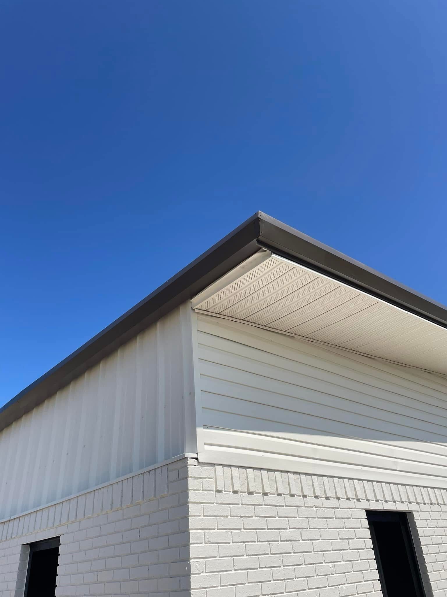 Exterior of a building with white siding, brick, and dark brown trim against a blue sky.