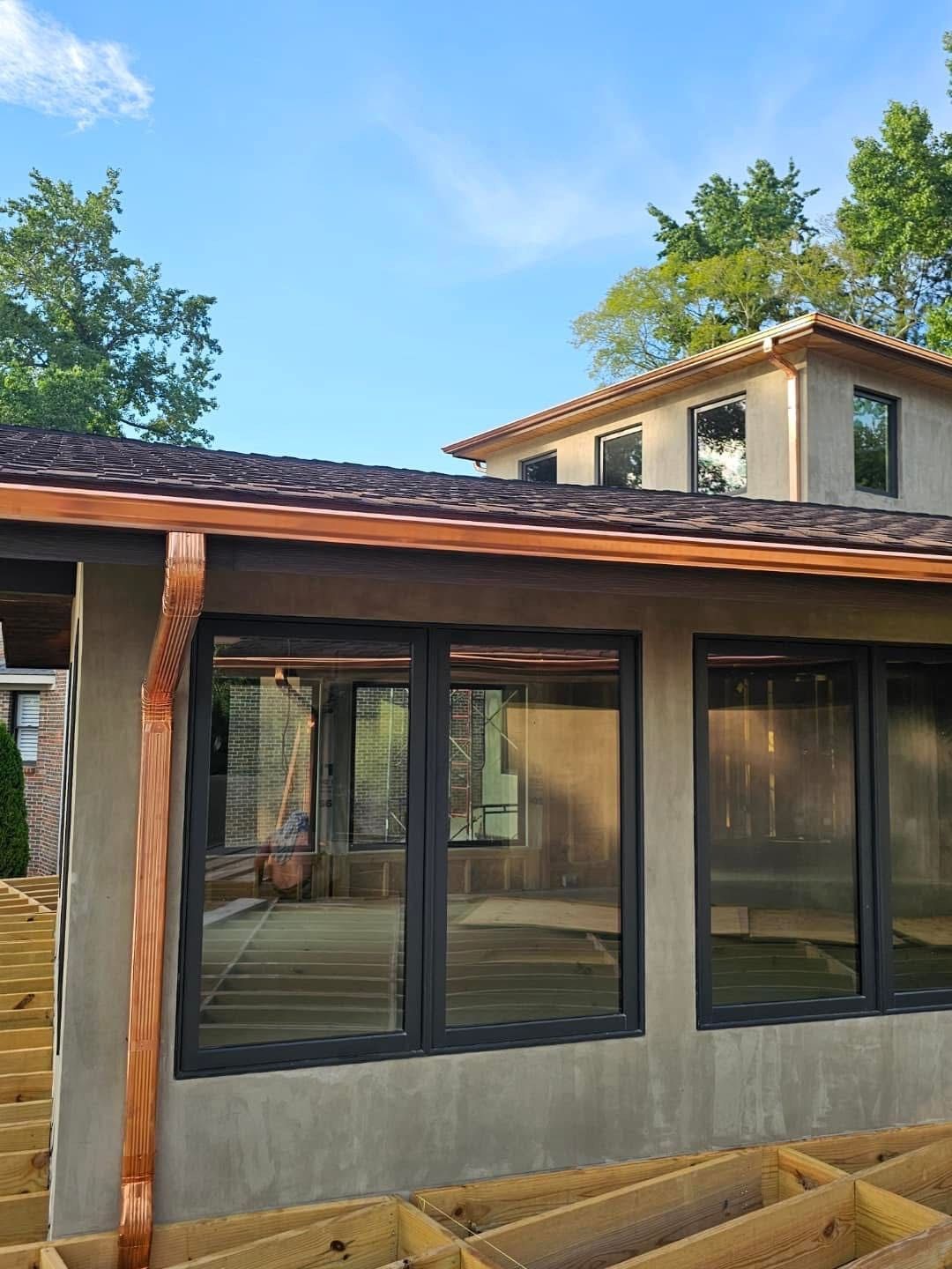 Exterior of a house with copper gutters, dark-framed windows, and a wooden deck under construction.