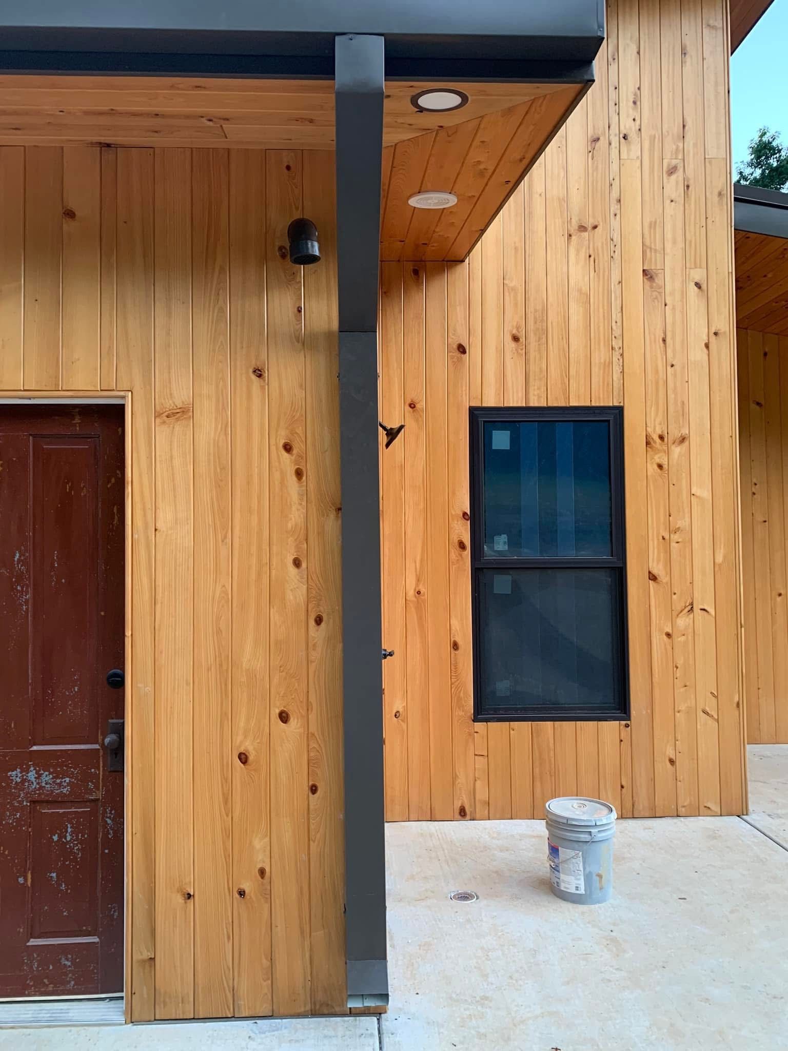 Wooden building exterior with a dark door, window, and grey support beam.