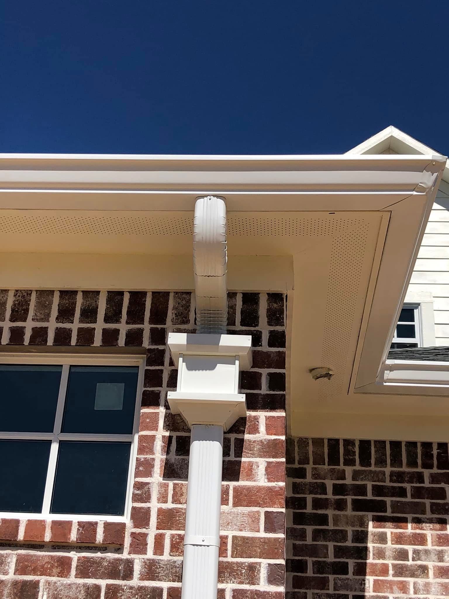 White gutter and downspout on brick building against a blue sky.