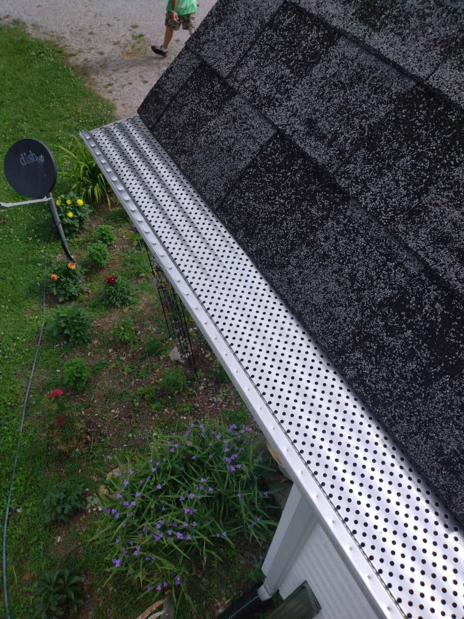 Gutter guard on a roof next to a garden and satellite dish. A person is visible in the background.