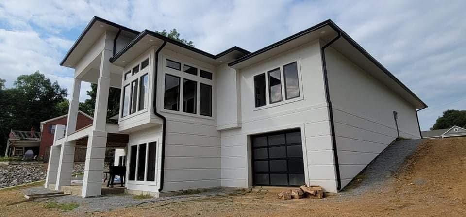 Modern white house with black trim, glass garage door, and windows under a cloudy sky.