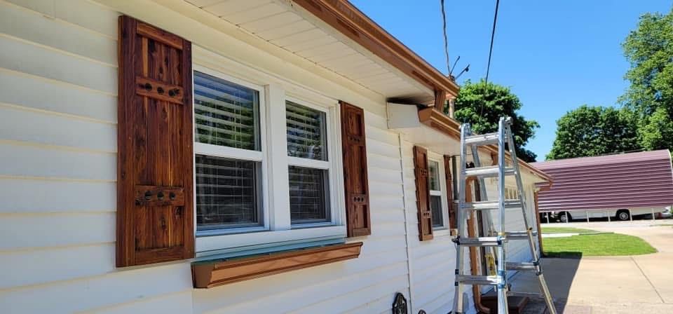 White house with brown shutters and a ladder propped against the side.