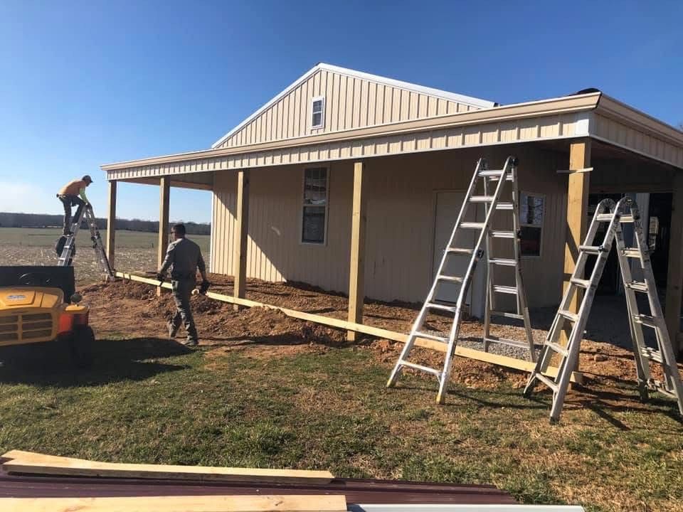 Construction workers building a beige-sided structure with a porch on a sunny day.