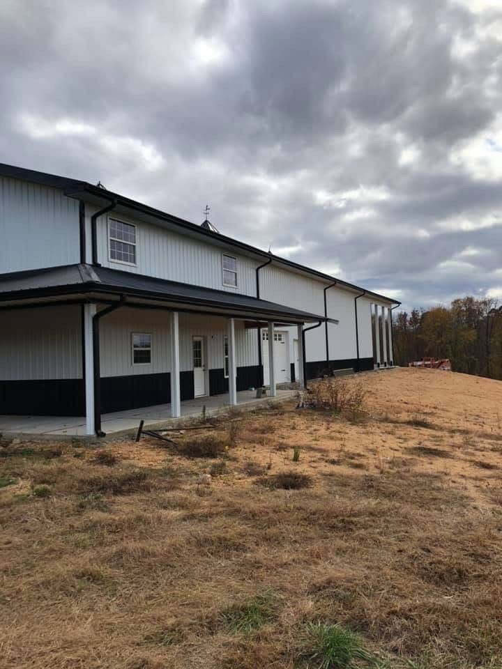 White and black barn with a porch, set on a hill under a cloudy sky.