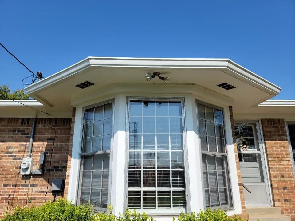 Brick house with bay window under a white eave. Blue sky in the background.