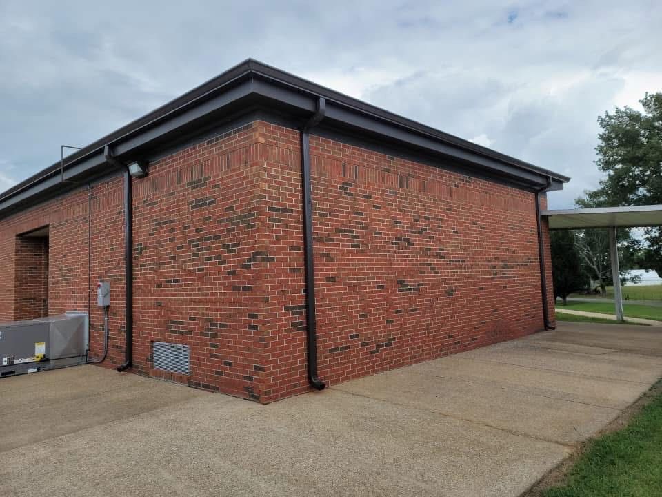 Red brick building with brown gutters and a concrete walkway on a cloudy day.