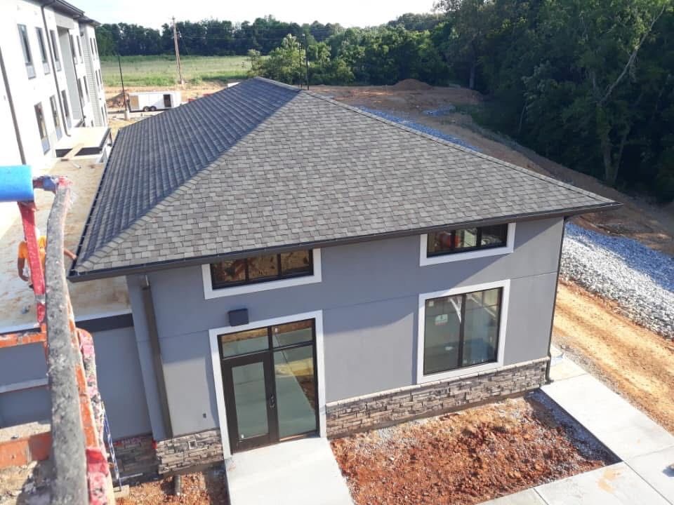 Gray building with dark roof, stone trim, glass door, and windows under construction.
