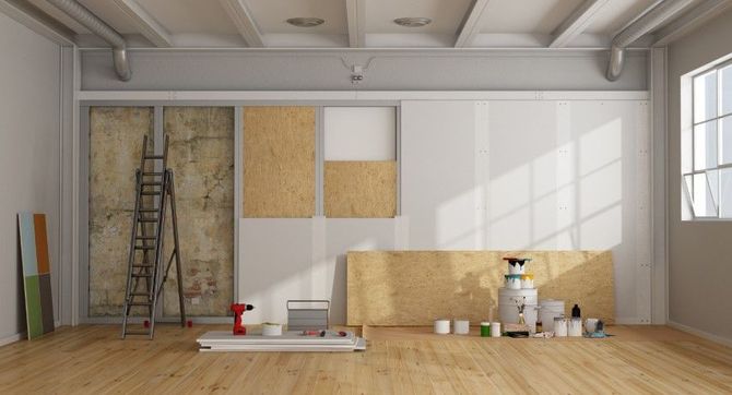 Bright empty room under renovation with ladder, paint cans, cardboard, and tools on the floor